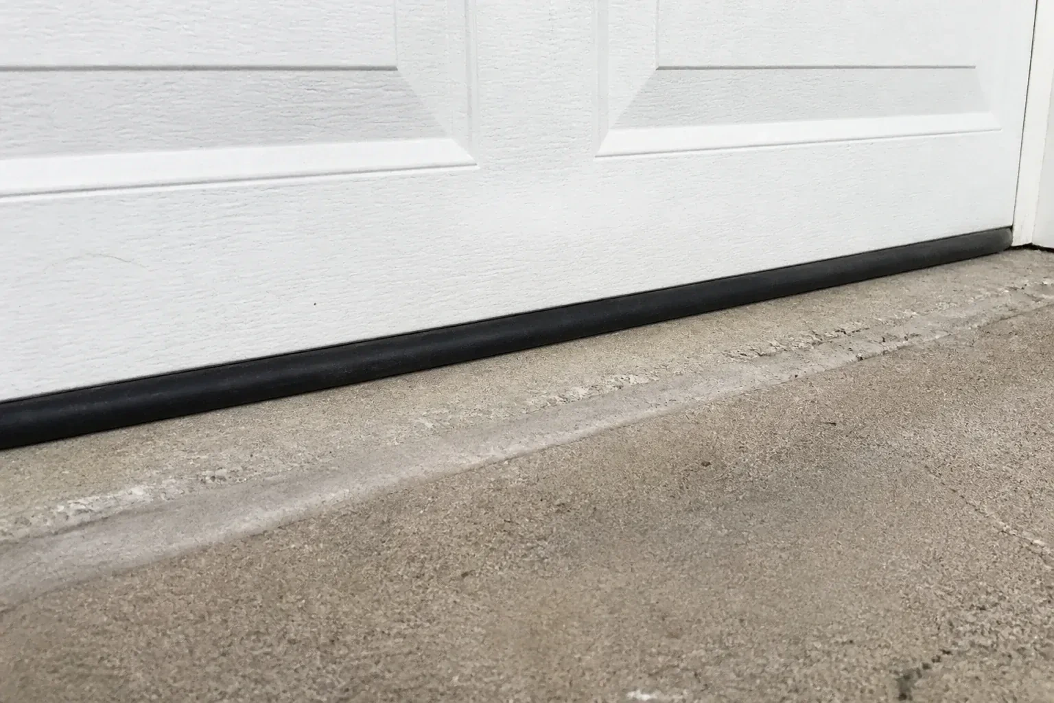 Black bottom seal along a closed white garage door at a concrete threshold. — Garage Door Bottom Seal Replacement, Port Robinson
