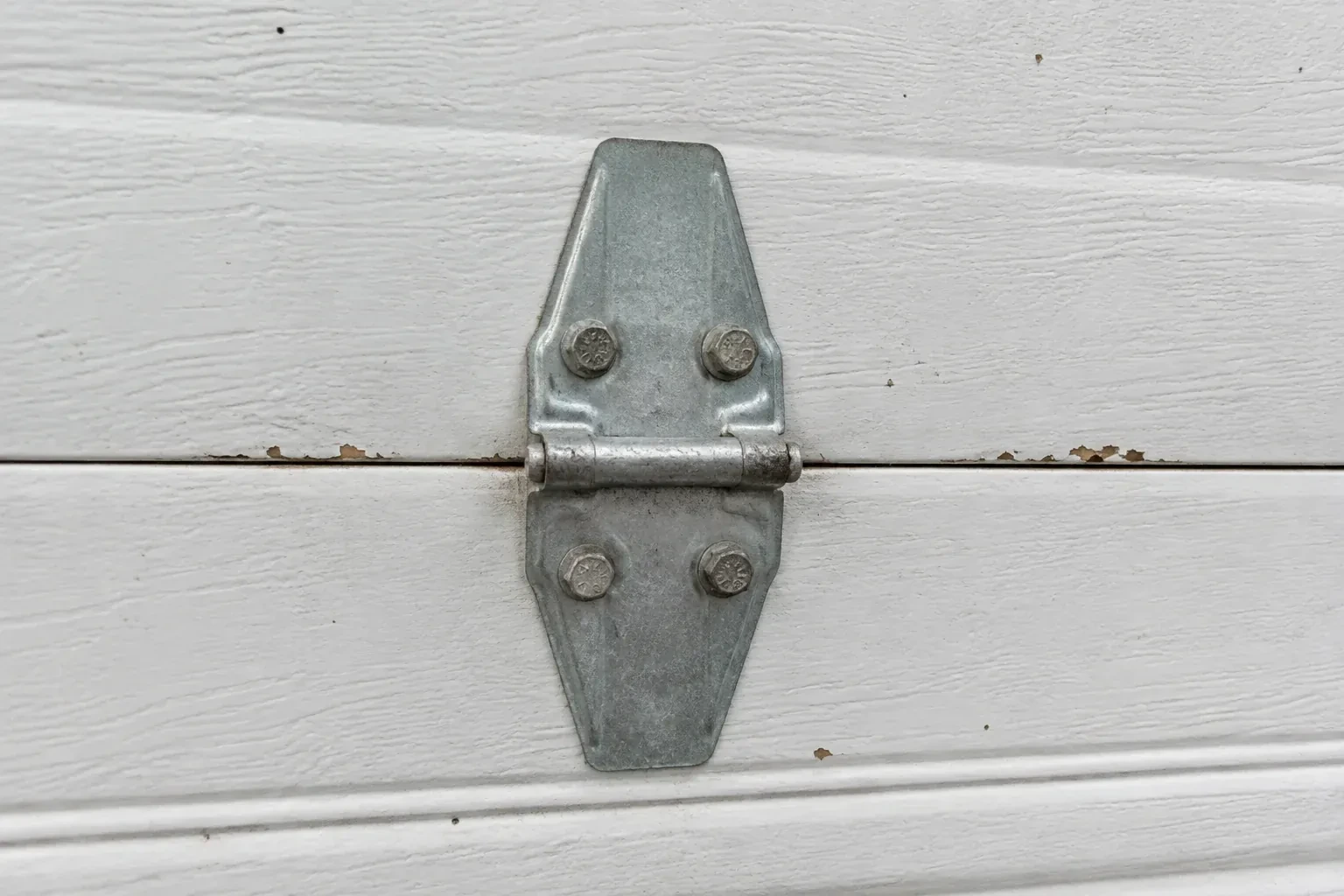 Metal center hinge across a seam in a white sectional garage door. — Garage Door Hinge Replacement, Thorold