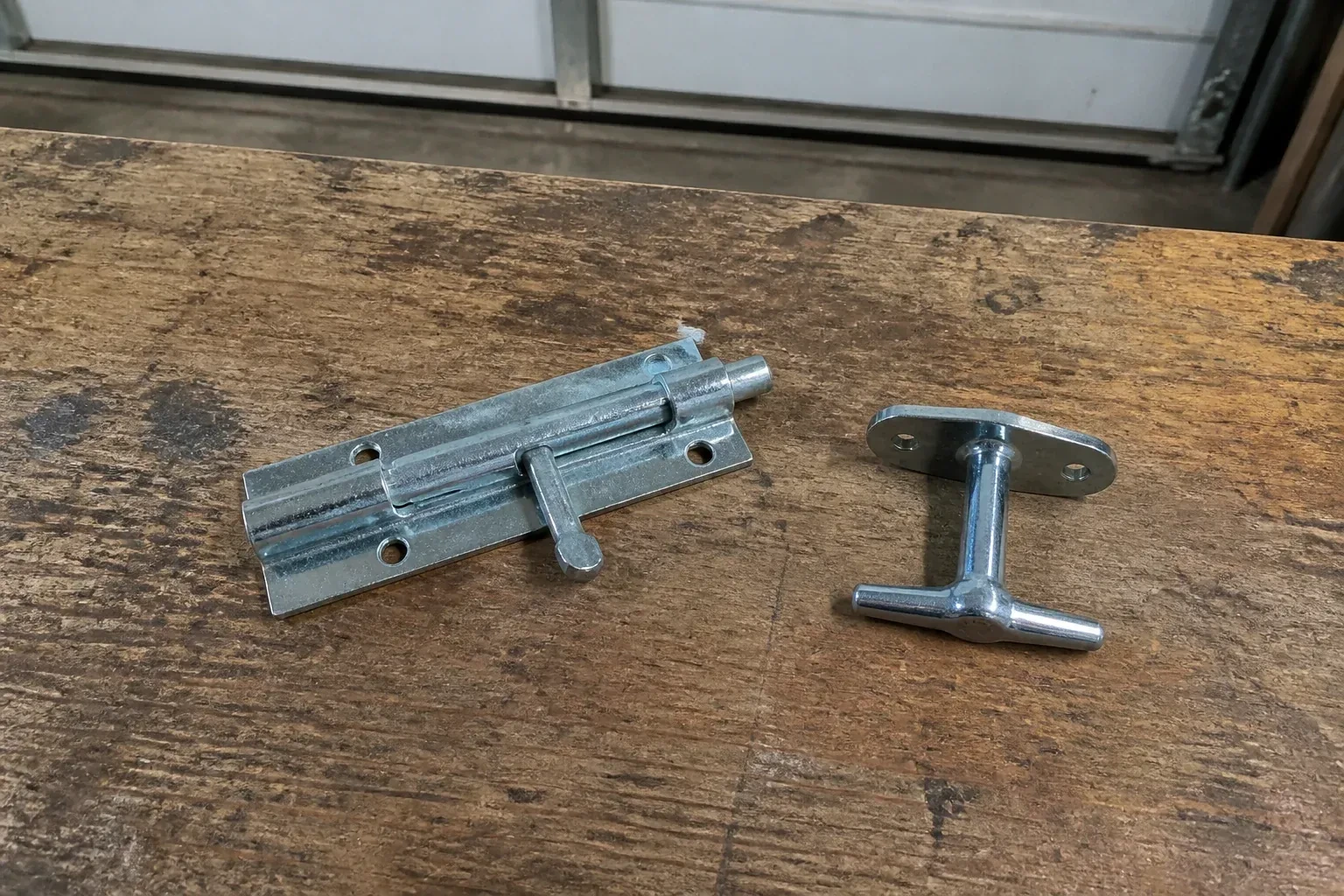 Detached slide bolt and T-handle on a wooden garage workbench. — Garage Door Manual Lock Repair, Beaver Dams
